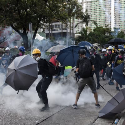 Demonstranter i Hongkong skyddar sig från polisens tårgaspatroner med paraplyn.