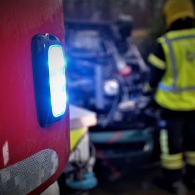 Paloauton vilkku ja taustalla onnettomuuteen joutunut auto. Kuvitus kuva, joka ei liity onnettomuuteen.