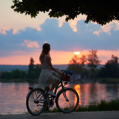 En kvinna på en cykel vid en sjö i solnedgång.