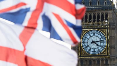 Brittiska och engelska flaggan fladdrar i vinden framför Big Bens urtavla vid brittiska parlamentet.