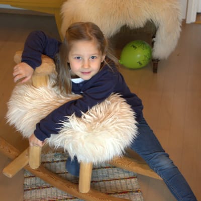 Flicka hänger på en liten gungstol som föreställer ett får.