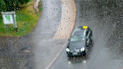 En taxi kör i regnet. Fågelperspektiv. Bilen syns genom ett regnvått fönster.