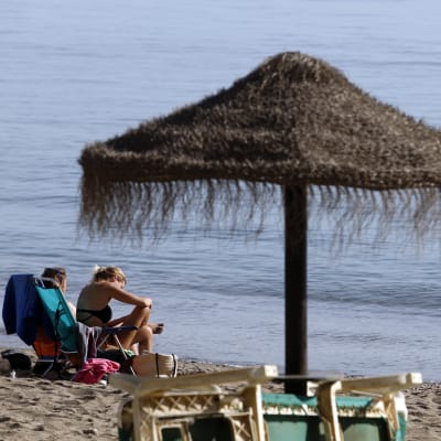 Två personer sitter i solstolar på stranden i Malaga.