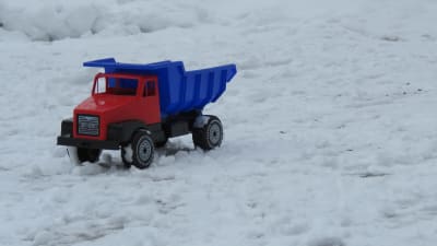 En leksaksbil i plast, röd och blå ute i snö. Vinter.