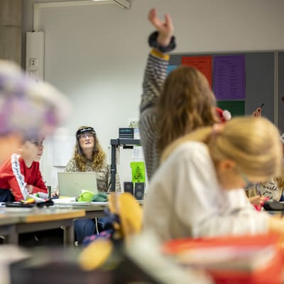 En lärare vid sitt skrivbord i en klass med elever.