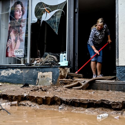 En kvinna städar ingången till en affär som skadats ordentligt i stormen i Tyskland