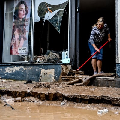 Nainen siivoaa tulvan tuhoaman liikkeen ovella.