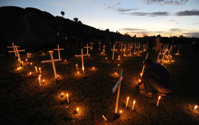 Levande ljus och vitmålade kors i mörkret i en sluttning. 