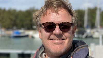 Glad man med rufsigt hår och solglasögon.