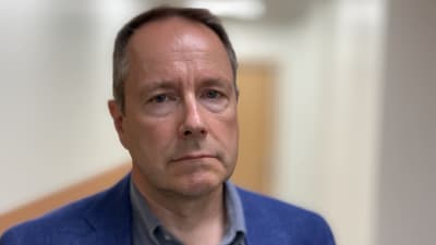 En man med blå kavaj och blå skjorta tittar in i kameran. 