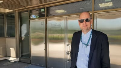 Man i solglasögon framför silverfärgade dörrar.