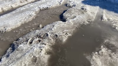 Stora vattenfyllda gropar på snöig väg.