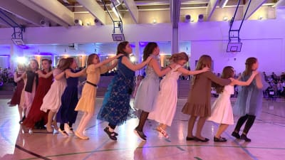 Flickor dansar letkajenkka i fina klänningar i Borgå idrottshall.