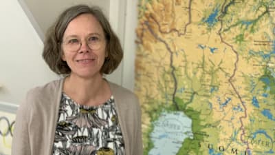 En kvinna med glasögon och kofta står framför en Finlandskarta