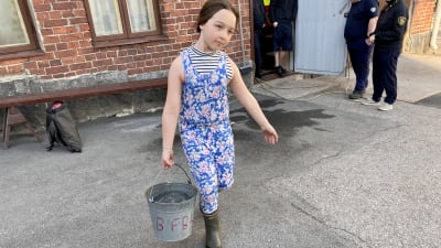 En flicka bär en hink med vatten.