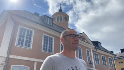 En man står framför Gamla rådhuset i Borgå. Det är en varm dag och solen lyser.