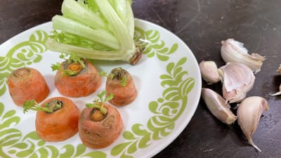 Porkkanoiden päät ja salaatin loppu lautasella vieressä valkosipuleita pöydällä
