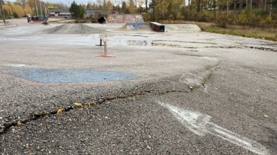 Närbild på asfalten i en skateboardpark. En ditmålad vit pil pekar mot en lång spricka.