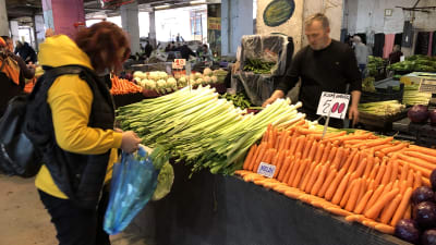 En kvinna plockar purjolök i en kasse vid ett stånd.