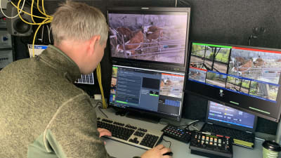 En eprson sitte ri en paketbils bakutrymme med många monitorer och teknik runt sig. 