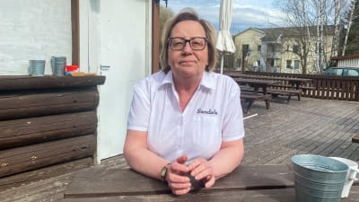 En kvinna i vita arbetskläder sitter på en tom restaurangterrass.