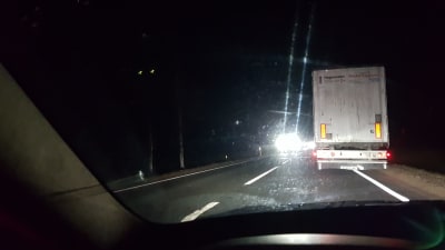 En mörk väg där bilisten möts av ljuslyktor från annan bil. Framför kör en lastbil. 