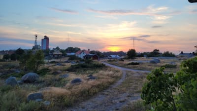 Em bil från Utö. På bilden syns en liten sanväg som leder fram till en fyr. Solnedgång mot havet i bakgrunden. 