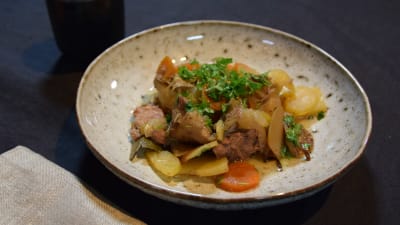 Ett ljust fat med en matportion. Matportionen är en kött- och potatisgryta med lite örter på.