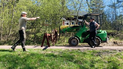 Två personer disktuerar aktivt, den ena står lutad mot en mindre grön traktor. 
