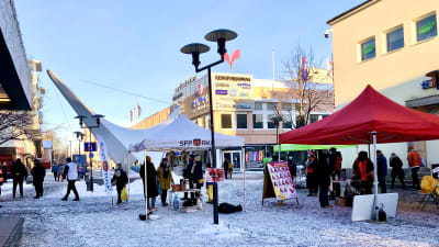 Lumisessa Kokkolan keskustassa on pystyssä vaalitelttoja ja niissä seisoskelee puolueväkeä.