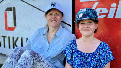 En mamma och en dotter i keps sitter vid ett staket.