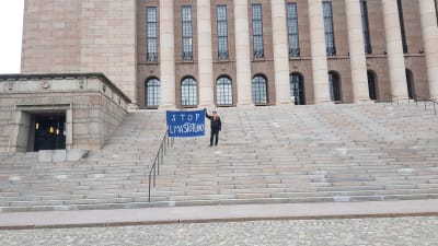 Ilmastoaktivisti Olavi Fellman seisoo Eduskuntatalon portailla yksin.