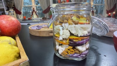 En glasburk fylld med skivade grönsaker som lök, betor, blomkål och svamp.
