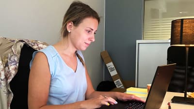 Elizabeth Harjunpää sitter och jobbar skriver på sin laptop. Hennes hår är fastsatt och hon har på sig en blå skjorta och blågult nagellack.