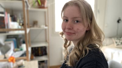 Tonårsflicka sitter vid sitt skrivbord, ler mot kameran.