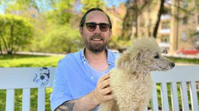 Philip Teir sitter i en blå skjorta med sin fluffiga hund i famnen i en park.