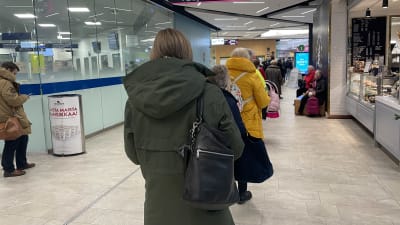 En lång rad människor står i kö i en gång i ett köpcentrum.