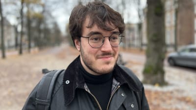 Närbild av mörkhårig man med glasögon som står i en allé