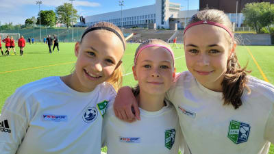 Tre glada flickor vid fotbollsplan.