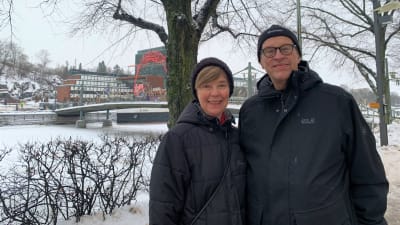 Raija och Timo står i svarta jackor vid Aura å i Åbo 