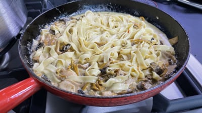 En röd gjutjärnsstekpanna med tagliatelle och en gräddig sås med kantareller och annan svamp.