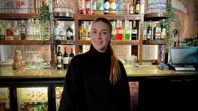 En kvinna står framför en välfylld bar.