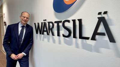 Man i kostym lutar mot vägg bredvid Wärtsilä logo.