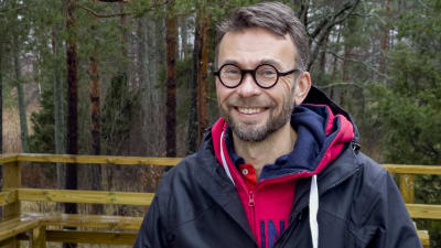 Ilkka Rissanen ute på en spång och altan gjord av tryckimpregnerat virke. Han ser glad ut.