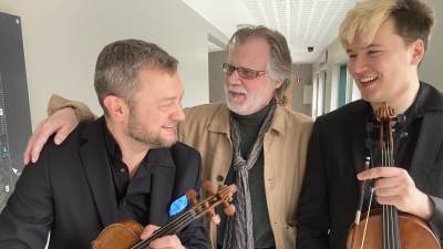 Kolme miestä, joista kahdella on viulut käsissään, hymyilevät Porin Promenadikeskuksen käytävällä.