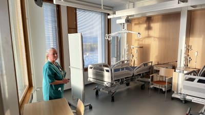 Ett tomt sjukhusrum med en kvinnlig sjukskötare i förgrunden. 