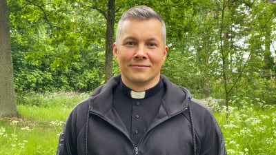 Kyrkoherde Daniel Björk står framför ett grönskande område. 