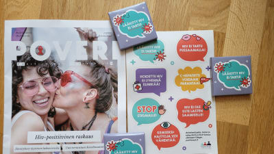 färgranna kondomfodral med texten W"medicinerad HIV smittar inte" och ett tidningsuppslag med information om HIV