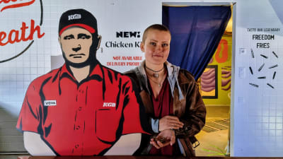 En kvinna står bredvid en figur föreställande Vladimir Putin som kassör i en snabbmatsrestaurang.