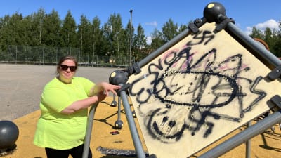 Grafitti målning på klätterställning. Kvinna i grönt och solglasögon står brevid. 